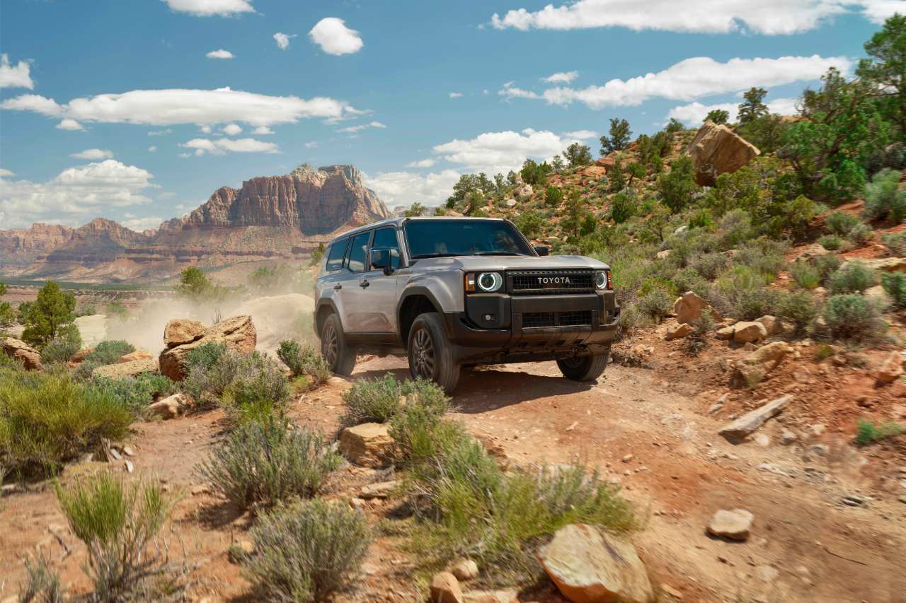 The 2024 Land Cruiser drives on a dusty road, off-roading in the desert.