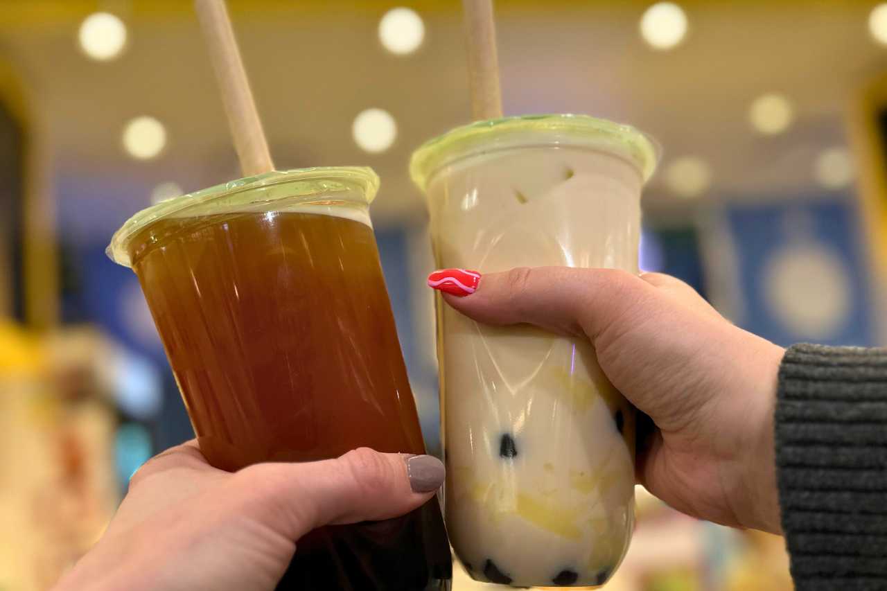 A fruit tea and milk tea are held by two women in front of Dream Tea House.