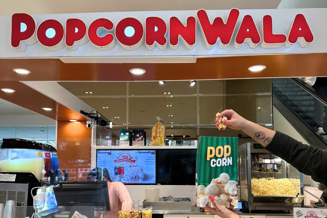 A woman holds up flavoured popcorn in front of a Popcornwala storefront in West Edmonton Mall.