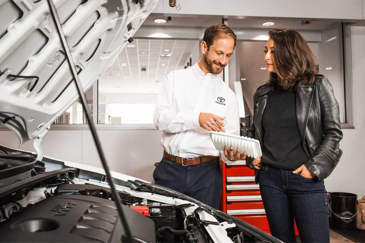 A service technician and client look under the hood of a vehicle during a service inspection.