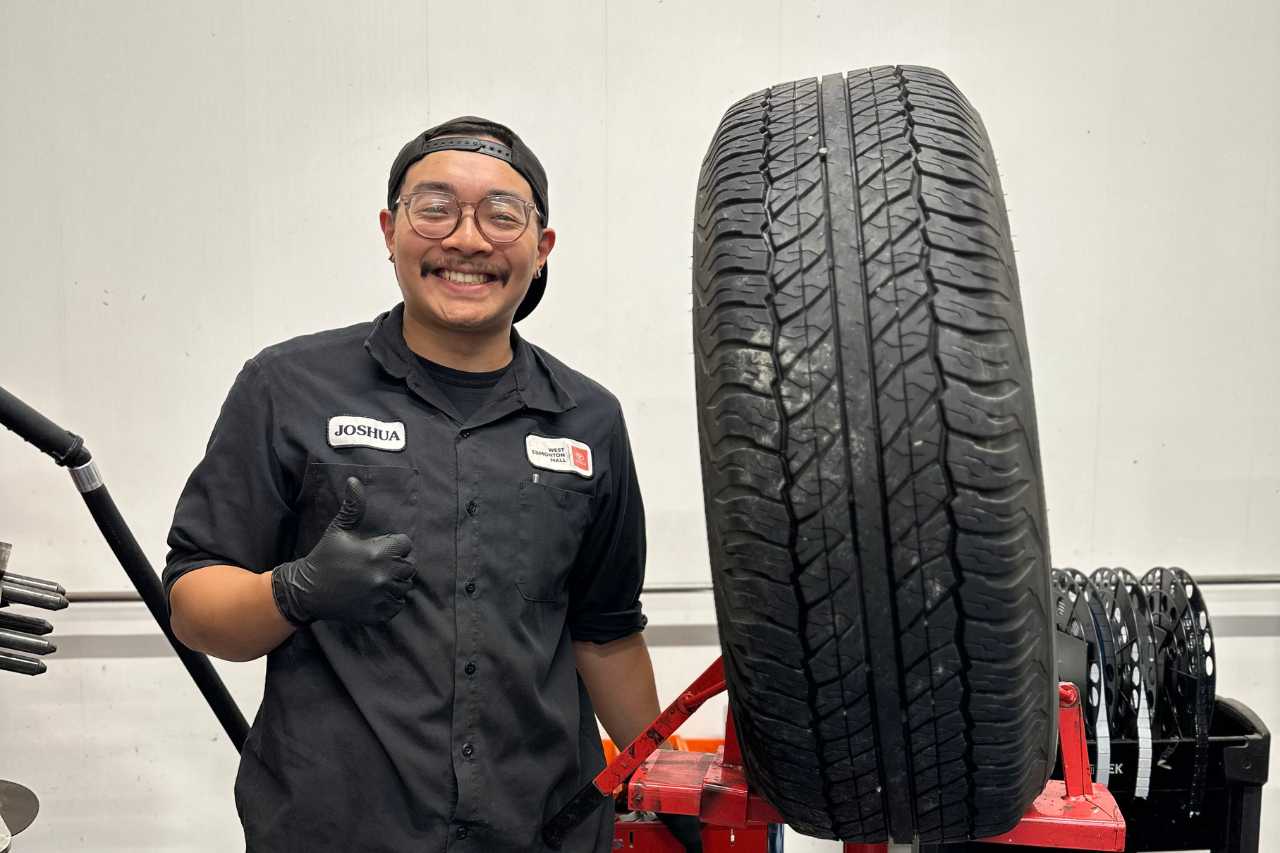 A Toyota service technician stands next to a new car tire.
