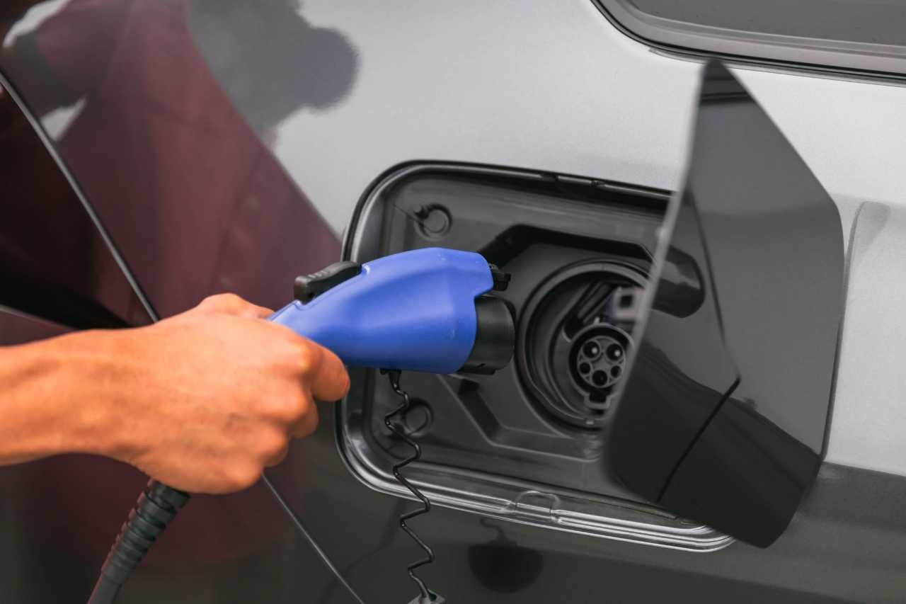 A caucasian man plugs an electric charging plug into an electric vehicle.