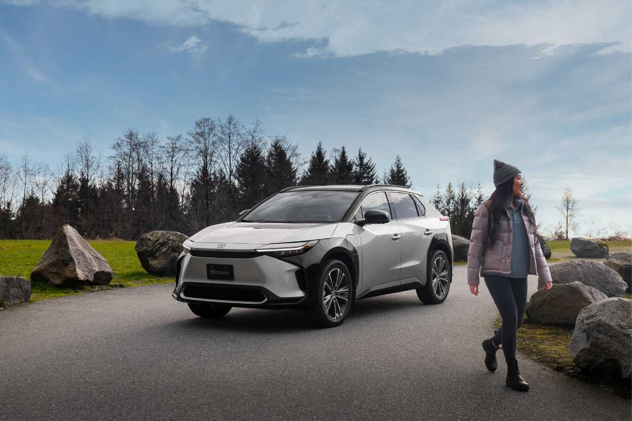 A woman walks away from a white Toyota bZ4X vehicle on a sunny day.