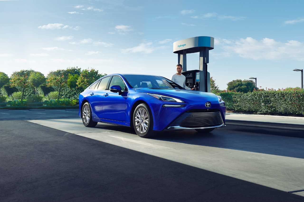 A man pulls up to an electric vehicle charging station in his blue Toyota Mirai.