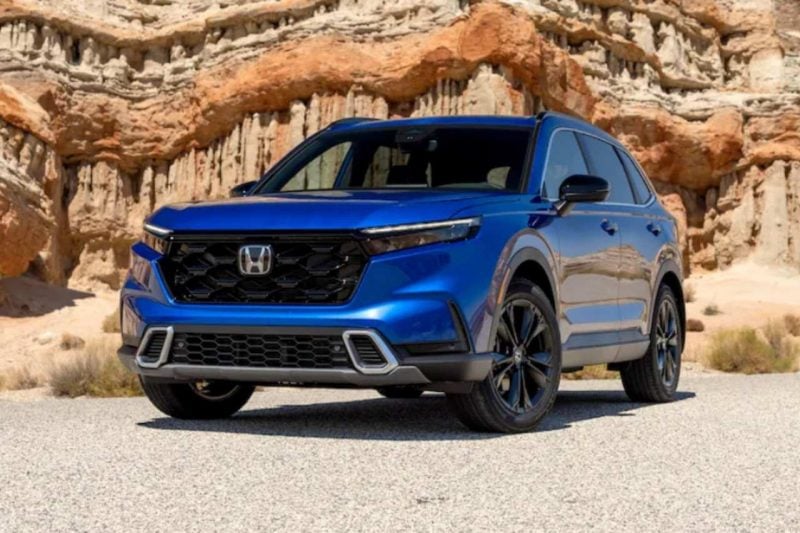 A 2024 Honda CR-V SUV in blue is parked in front of a rock formation wall.