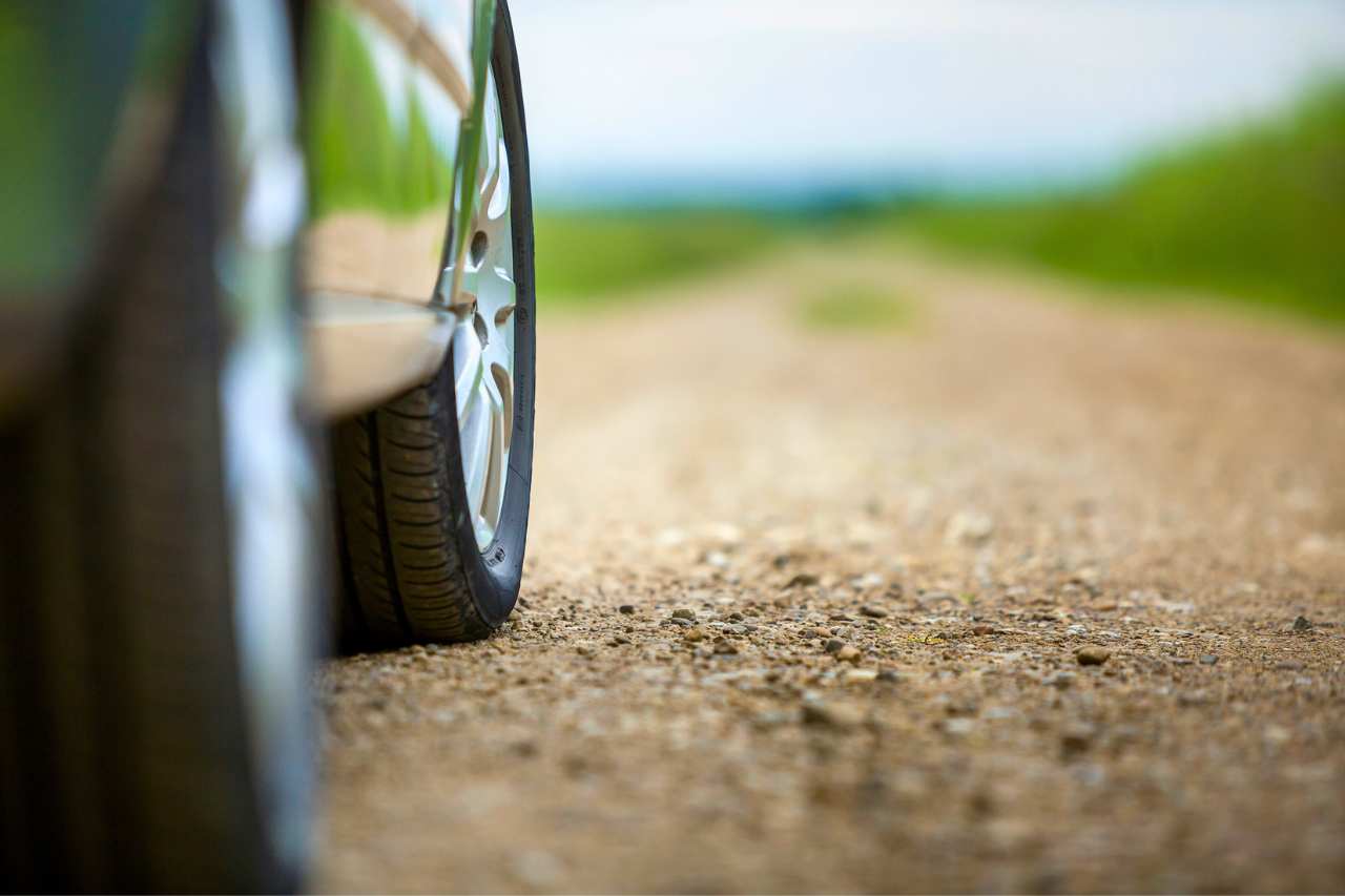 A vehicle drives on all-season tires on a sunny day on a dirt and grass road.
