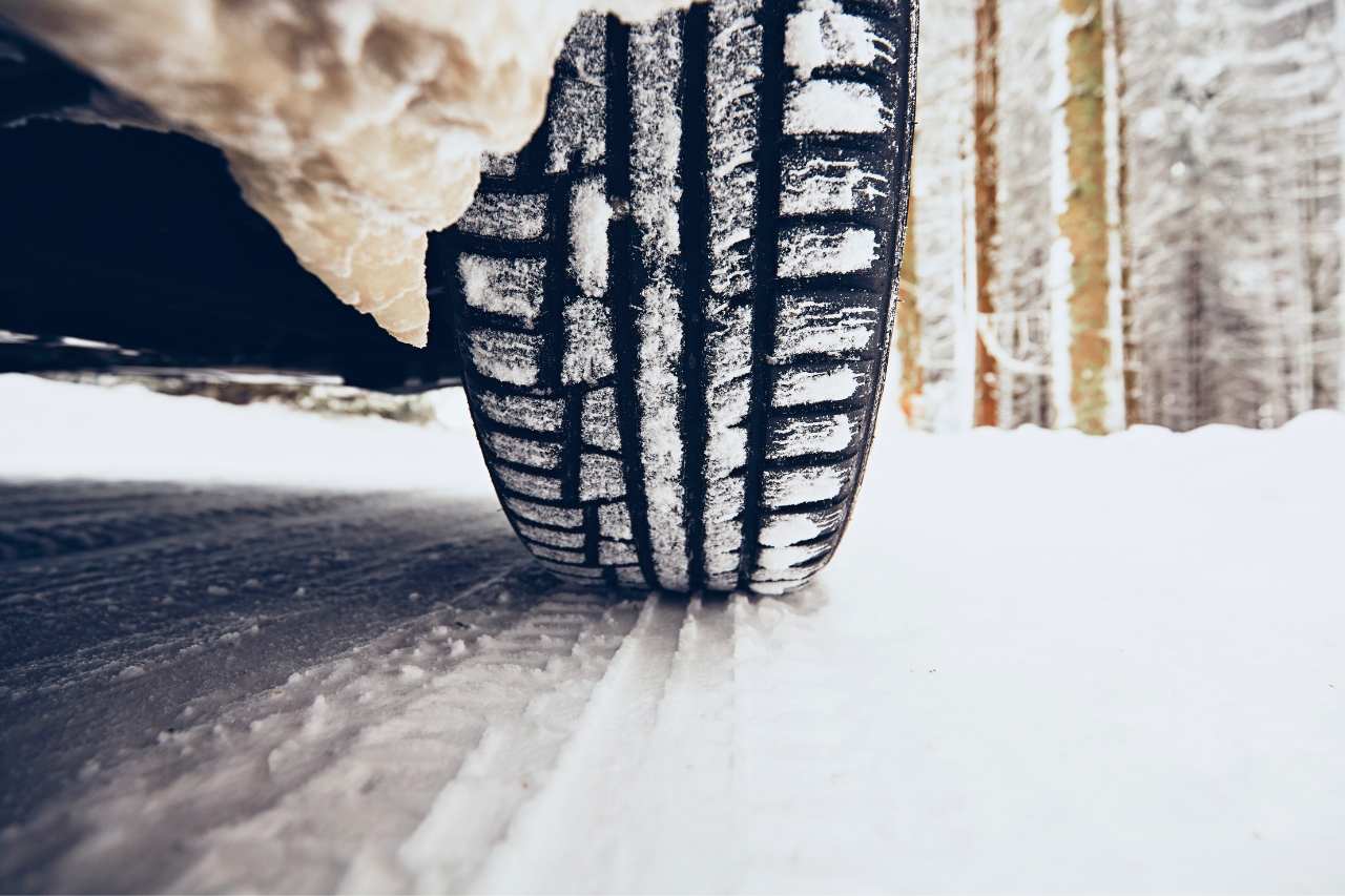A vehicle drives on winter tires on a snowy road in the forest, with snow packed behind the wheels.