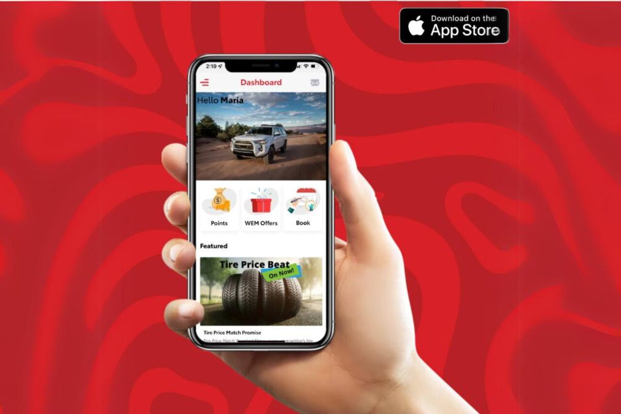 A hand holds up a phone in front of a red background, showcasing the West Edmonton Mall Toyota app and Tire Price Match deals available.