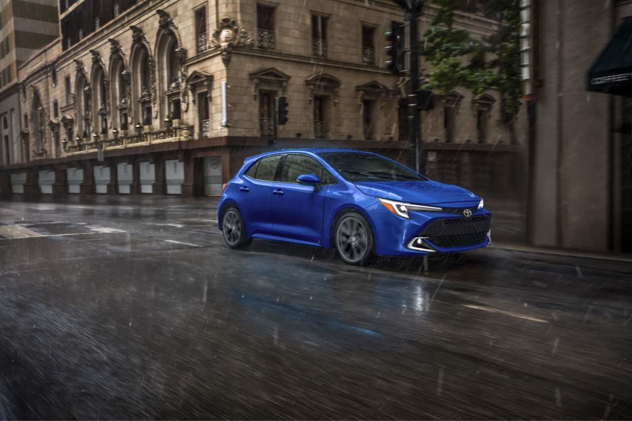 The 2025 Toyota Corolla Hatchback in blue drives down a rainy city street.