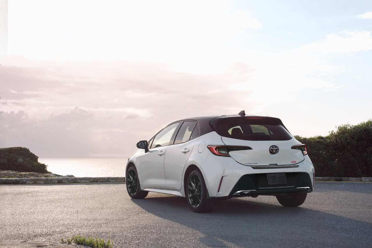 A white hatchback is parked in an empty parking lot overlooking the ocean.