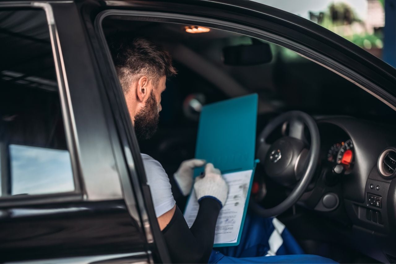 A mechanic writes on service papers while working on a customer's vehicle.