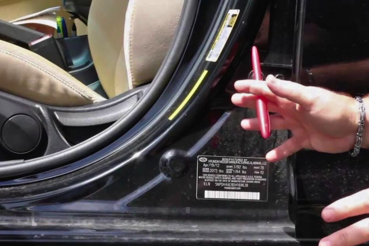 A picture of a Caucasian man's hands pointing towards the VIN sticker on a car door.