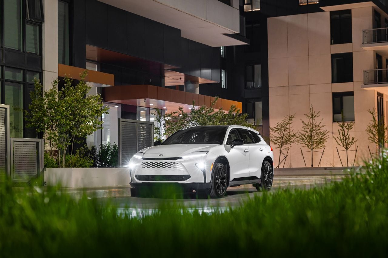 A white Toyota SUV with sleek highlights is parked in front of a modern apartment building at night.