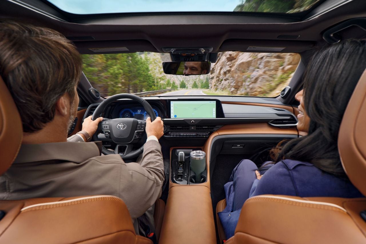 A couple drive in a Toyota SUV with a saddle tan leather interior, heated steering wheel and large multimedia screen.