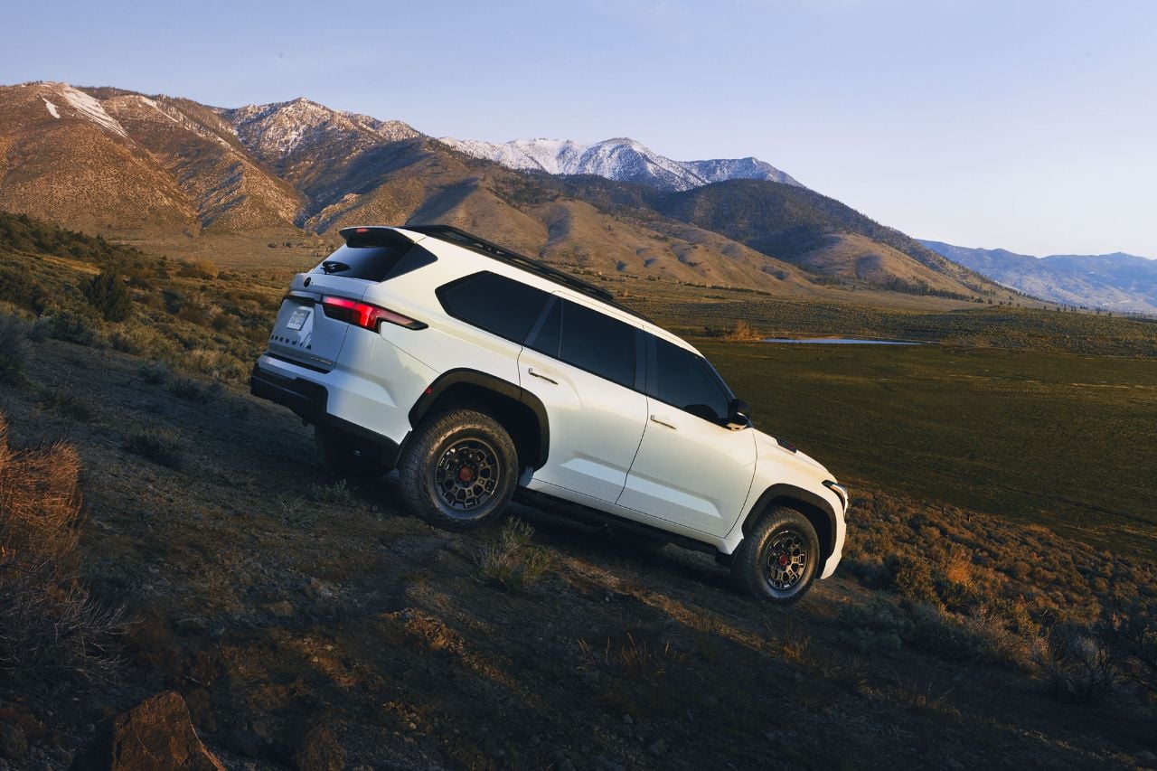 A white 2025 Toyota Sequoia SUV is parked on a downhill slant on a sunny mountain hill, showcasing its sporty abilities.