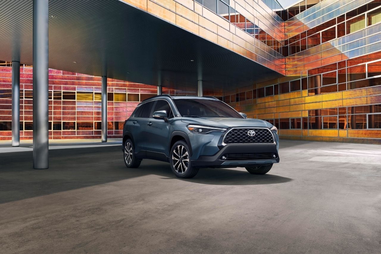 A brand new Corolla Cross SUV is parked outside a colourful modern building.