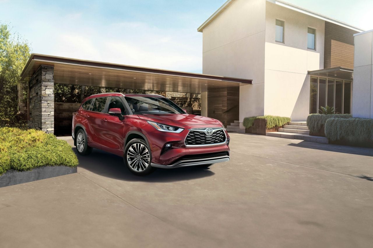 A red SUV is parked outside of a modern home on a sunny afternoon.