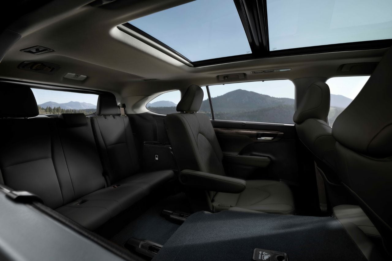 An interior view of the 2025 Toyota Highlander three-row SUV, showcasing its passenger space and panoramic moonroof.