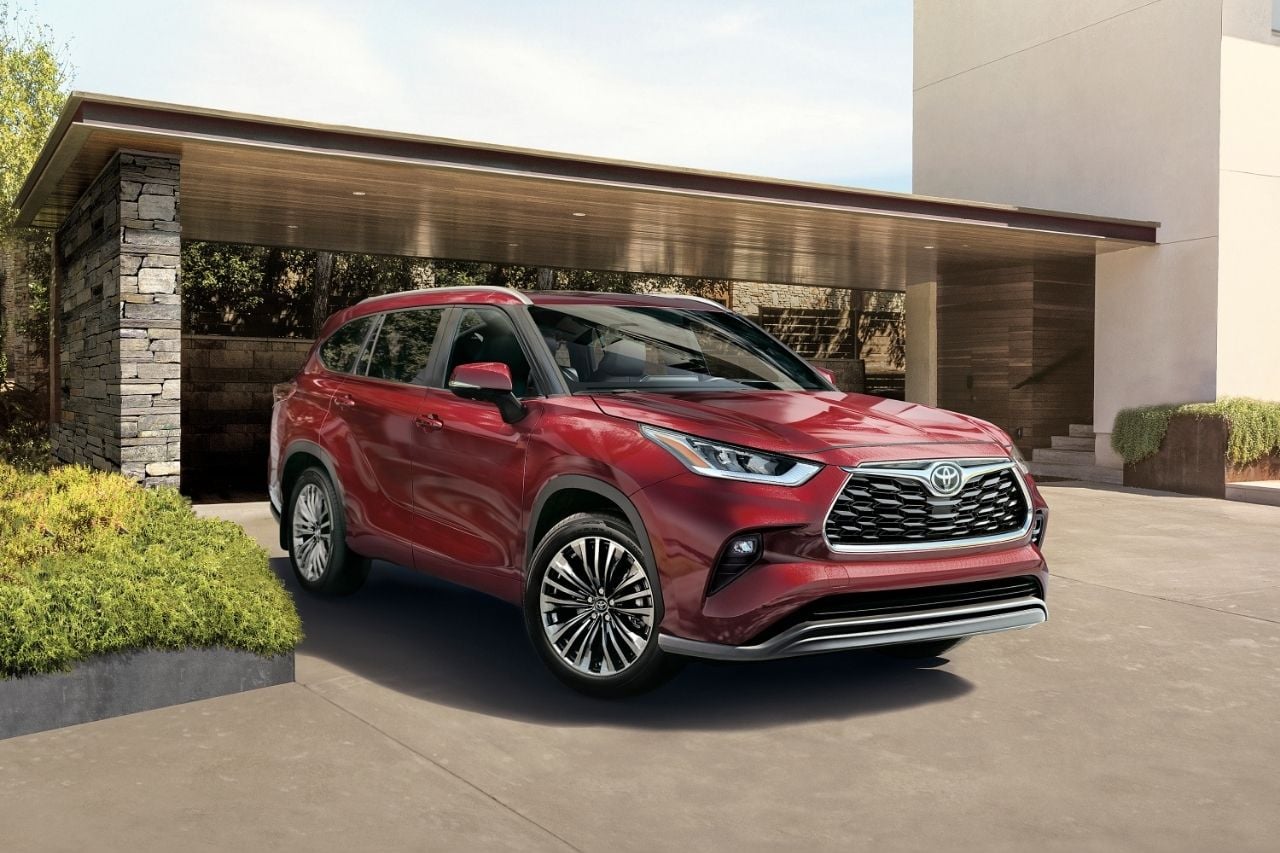 The new 2025 Toyota Highlander in red is parked outside a beautiful modern home on a sunny day.