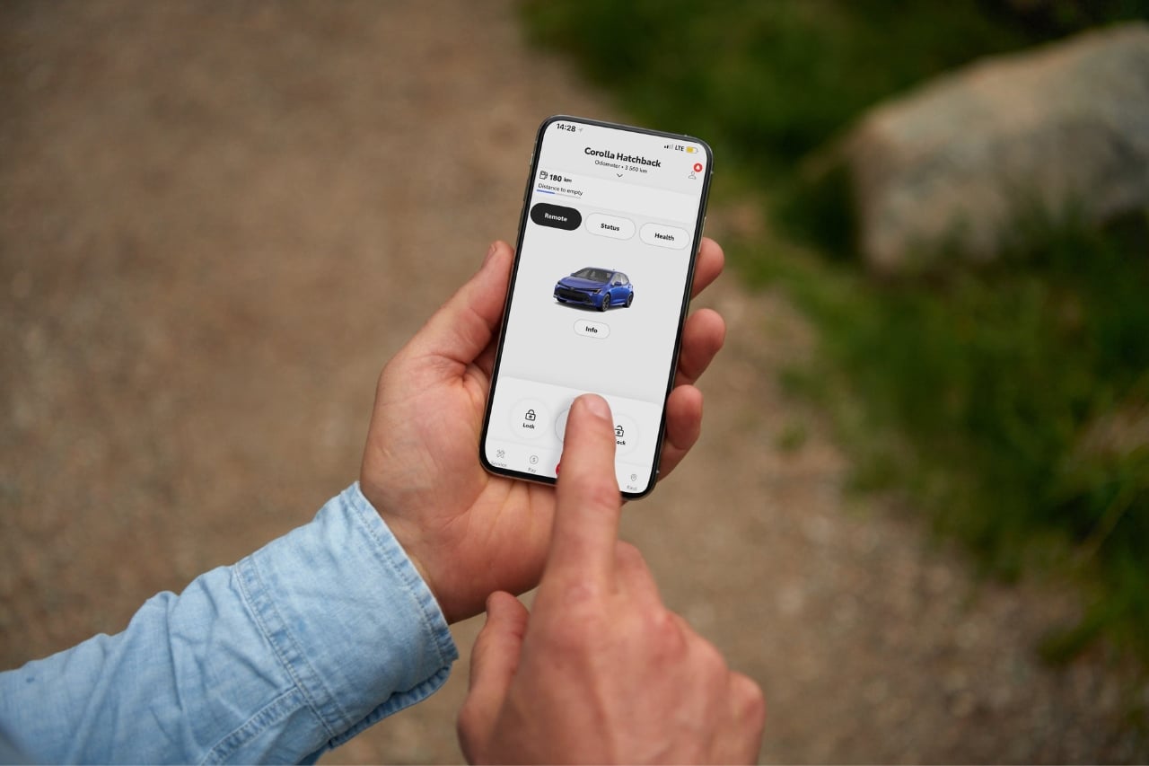 A man in a blue shirt holds his smartphone and explores the Toyota Remote Connect app that's connected to his Toyota Corolla.