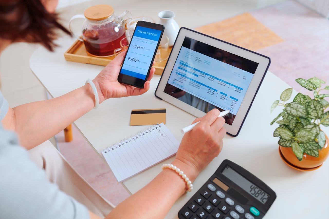 A person opens up their online banking apps on an electronic tablet and phone to pay their bills on time.