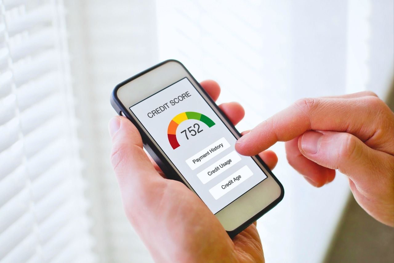 A person checks their credit score online on their mobile phone in front of a window with lots of natural light.