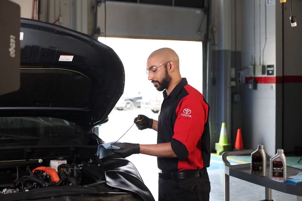 A Toyota service technicians check the engine oil levels while performing maintenance on a car.