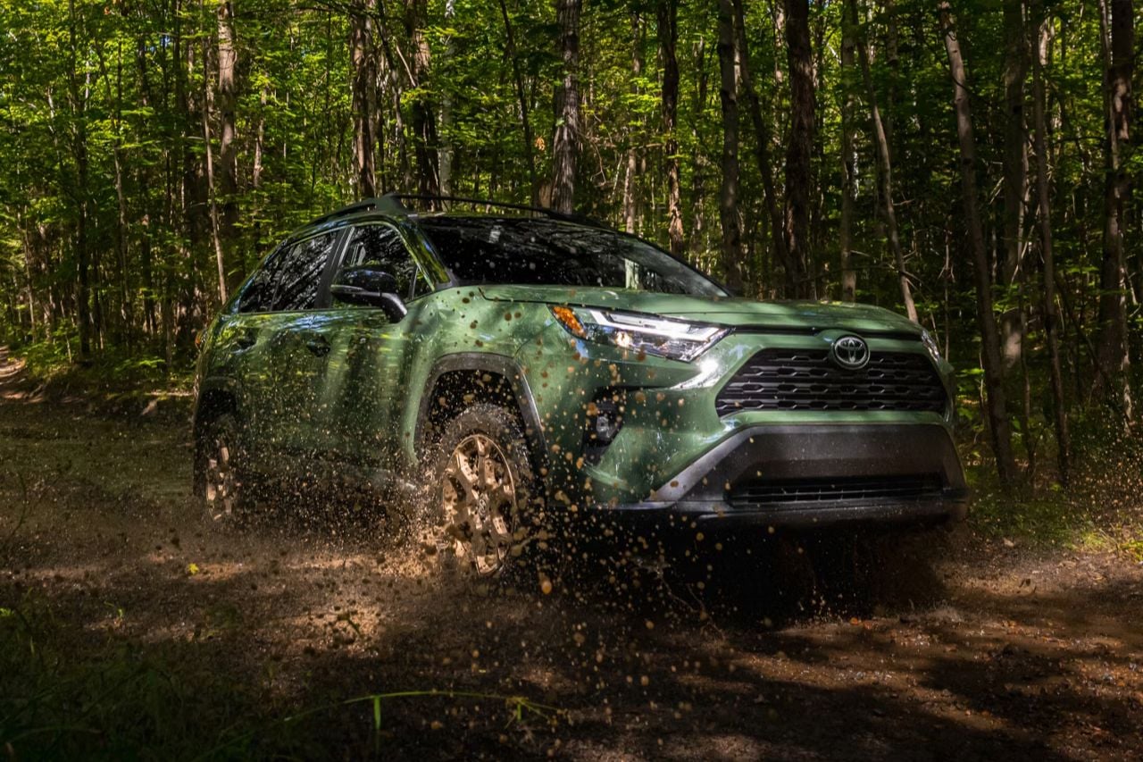 A muddy RAV4 in a dark green colour drives down a muddy forest road.