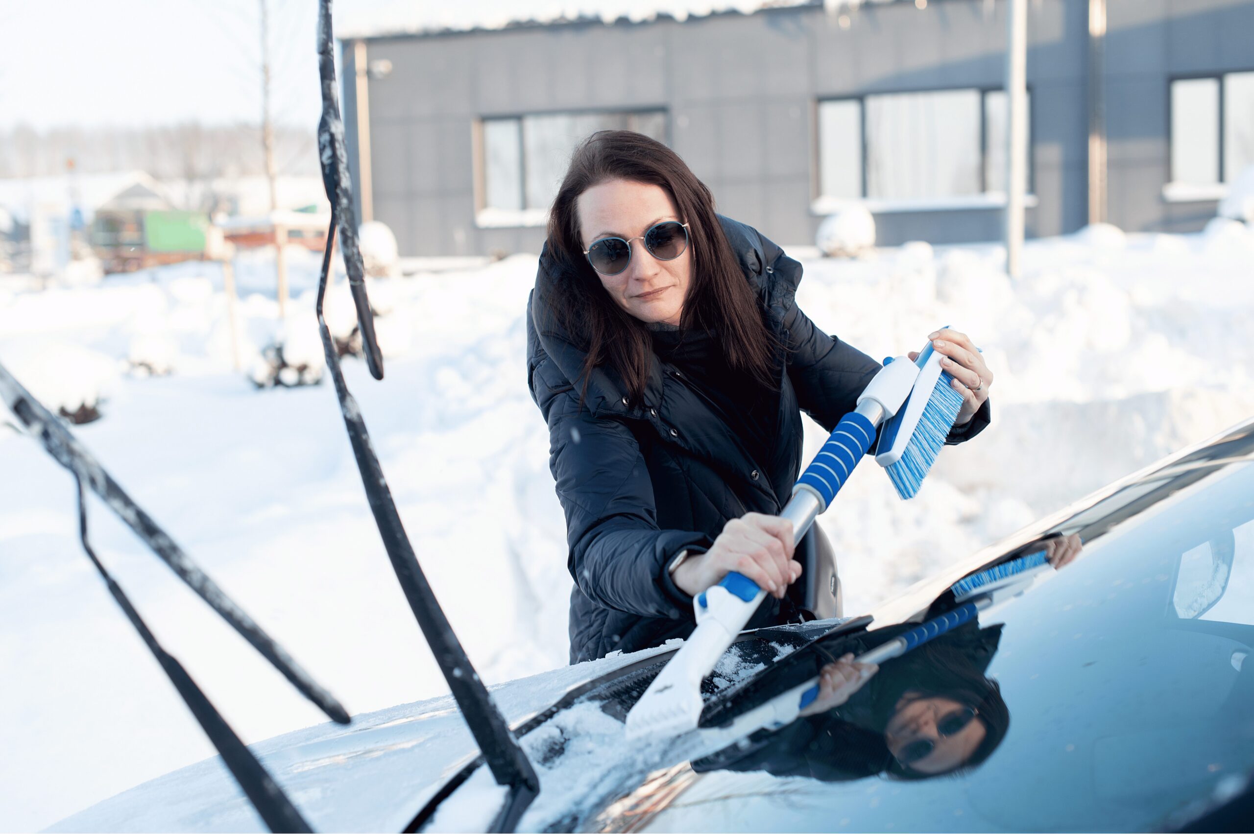 woman removing snow from wind shield to prepare for winter driving