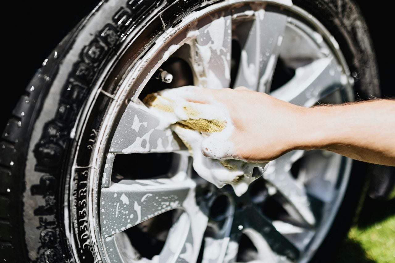 A person washes down their car tires with a soapy sponge. Car detailing is one of our car maintenance tips for spring.