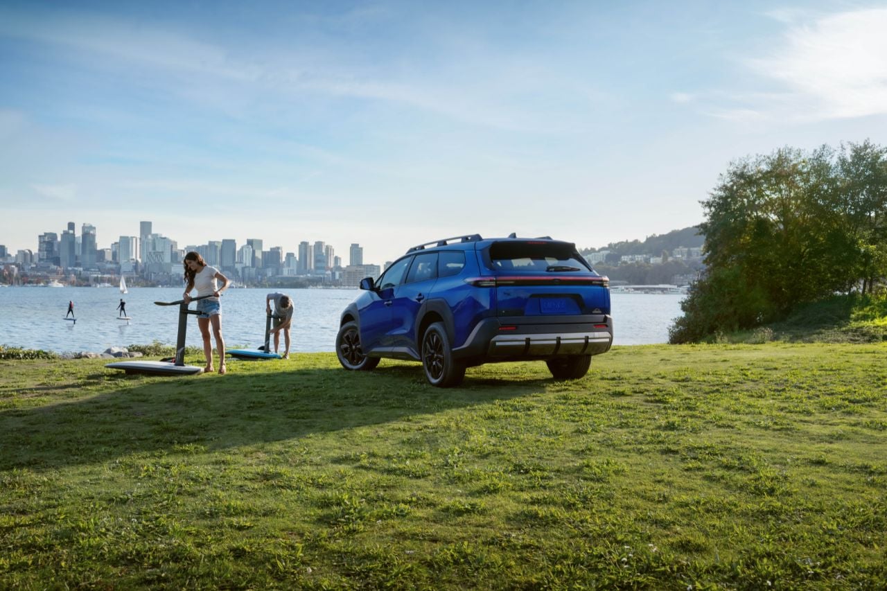A Toyota bZ vehicle is parked on green grass next to a large lake on a sunny day.