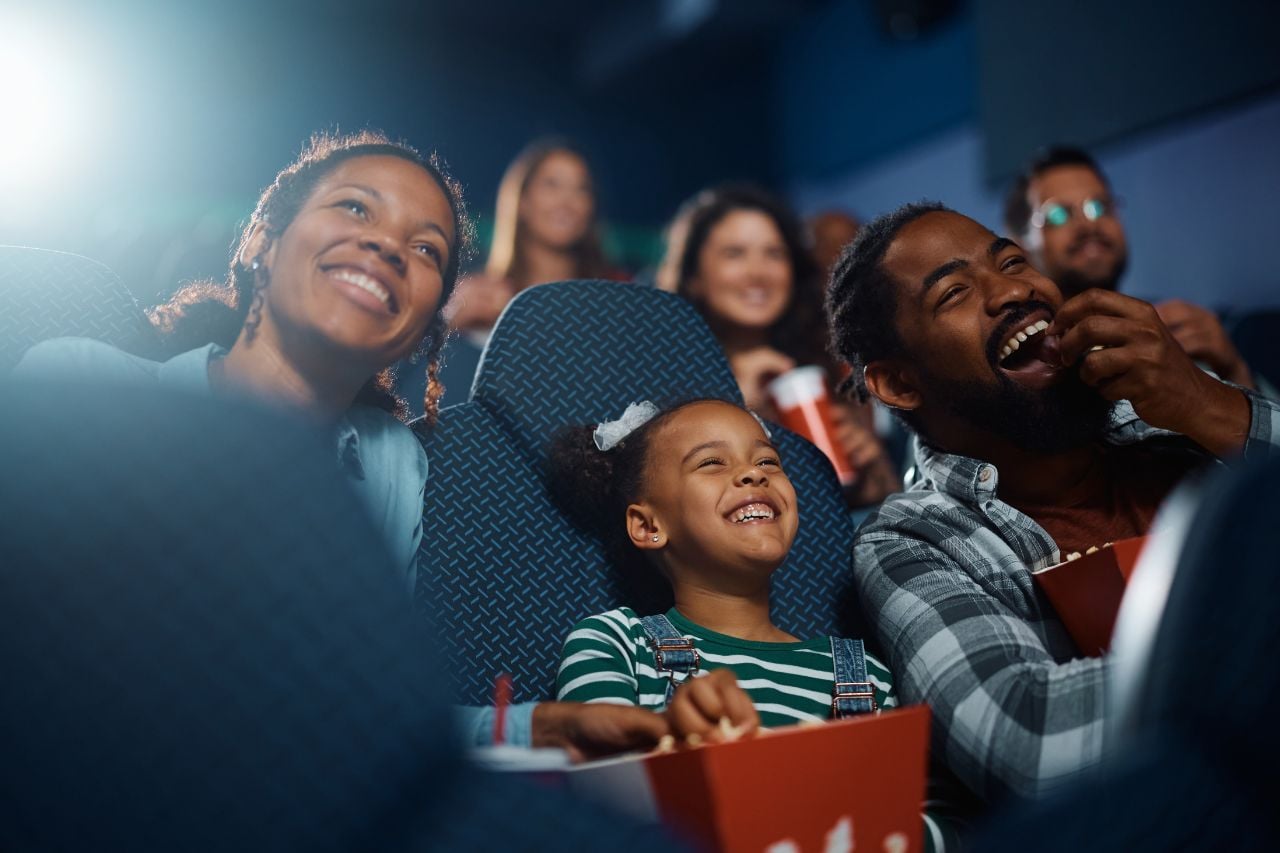 A young African-American family sit in the cinema and watch a movie.
