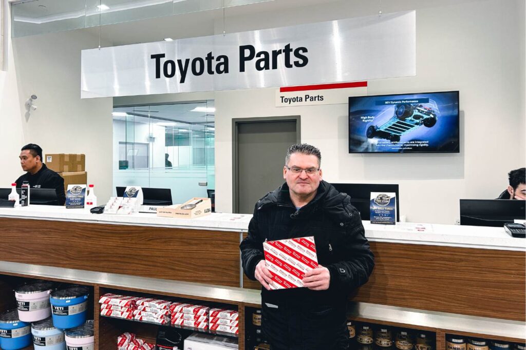 A customer smiles at the camera and holds a Toyota Genuine Parts car filter. He has used the Parts Drive-Thru to quickly collect his order.