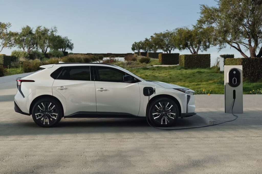 A white Toyota bZ SUV is plugged up to an electric vehicle charger in a modern outdoor garden.