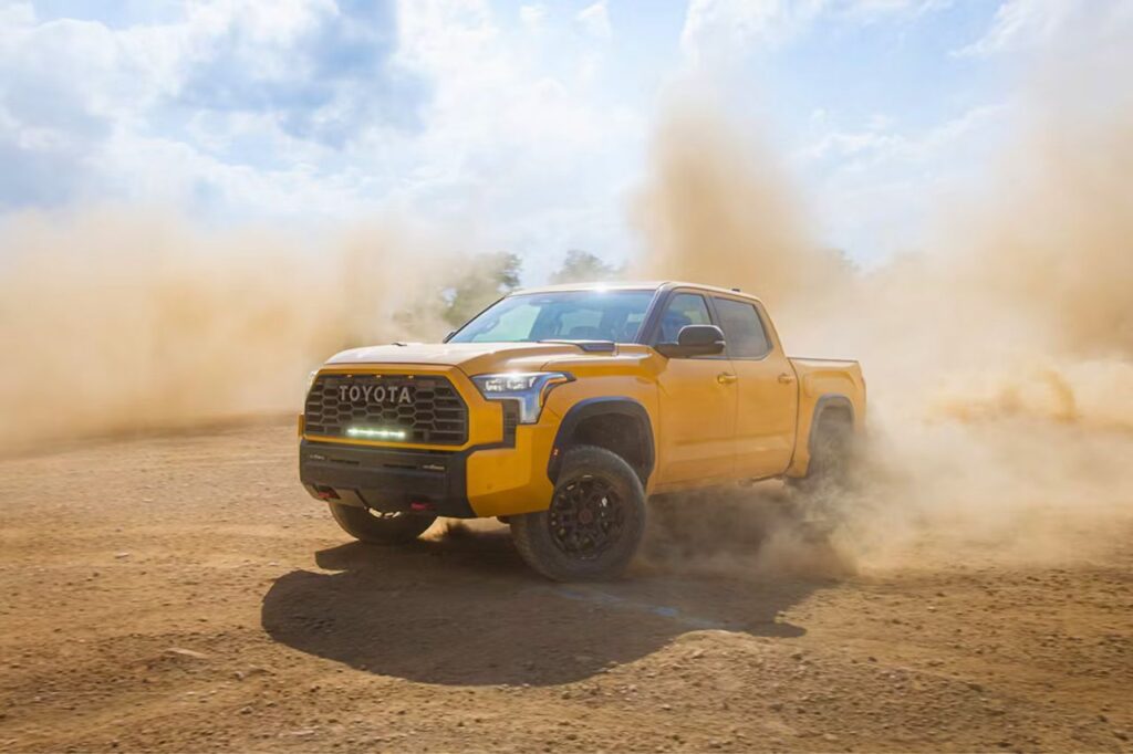 The 2027 Toyota Tundra TRD Pro in the exclusive Honeycomb colour. The truck drives through a dusty field.