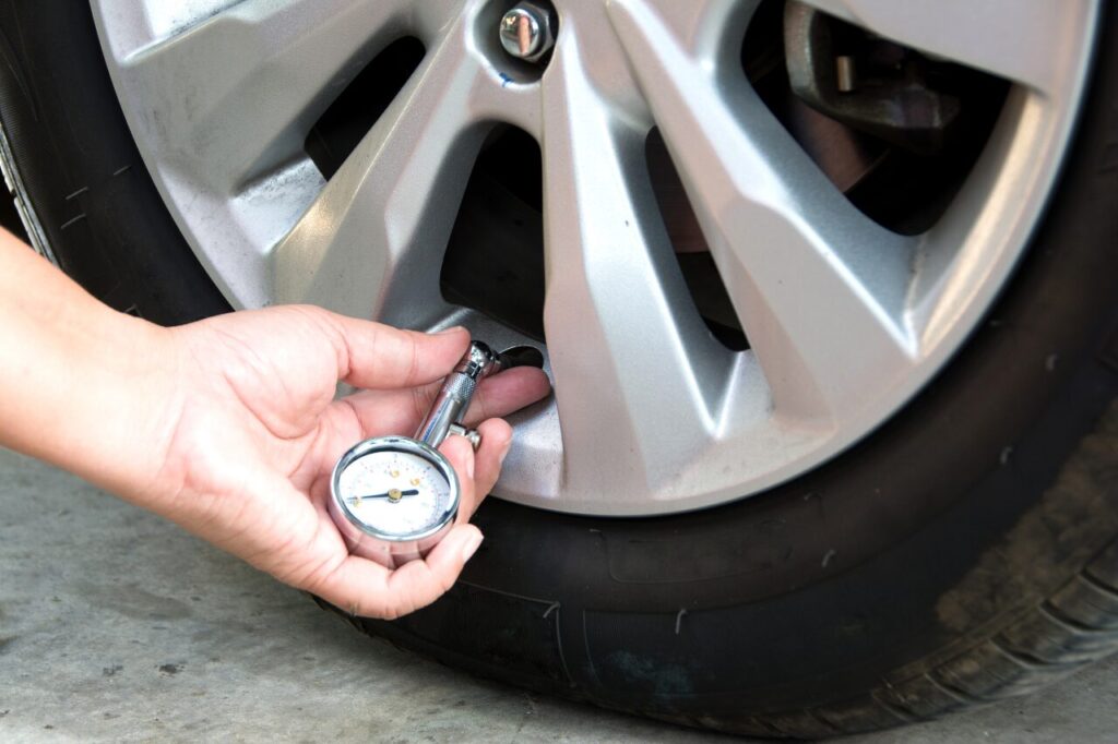 Summer Car Maintenance Tips to Keep You on the Road-2 A white man uses a tire pressure gauge to check his tire pressure on his driveway as part of his summer car maintenance routine.