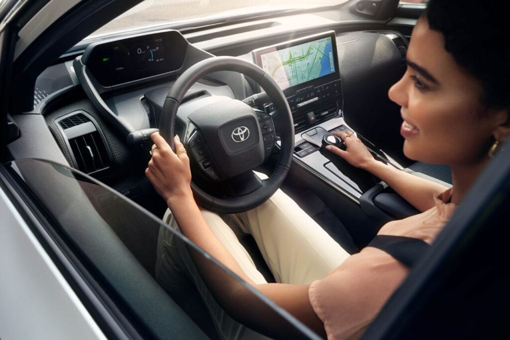 Summer Car Maintenance Tips to Keep You on the Road-3 A Caucasian woman drives a Toyota bZ on a sunny afternoon. Her hands hold the steering wheel.