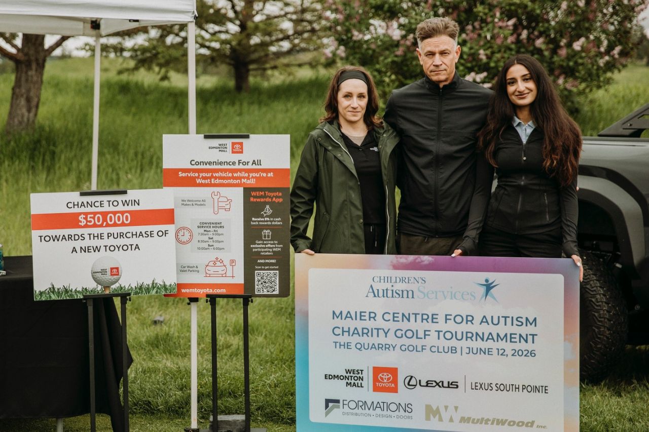 3 West Edmonton Mall team members stand at their booth at the 13th Annual Maier Centre for Autism Charity Golf Tournament and hold up a tournament sign.